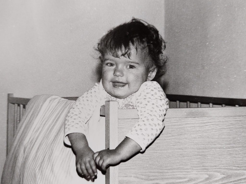 Zdjęcie z rodzinnego albumu odnalezione podczas porządkowania i sortowania zdjęć przedstawiające małe dziecko w łóżeczku. 